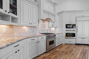Kitchen featuring stainless steel appliances, light stone counters, tasteful backsplash, and dark wood finished floors