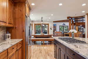 Kitchen featuring light stone counters, stainless steel appliances, light wood finished floors, wood finish cabinetry, and hanging light fixtures