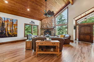 Living room featuring light wood-style flooring, a vaulted wooden ceiling, a ceiling fan, a stone fireplace, and recessed lighting