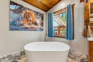 Bathroom with marble tiled flooring, vanity, a vaulted wooden ceiling, and a freestanding bath
