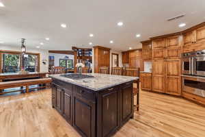 Kitchen with a kitchen bar, stainless steel appliances, light stone countertops, and light wood finished floors