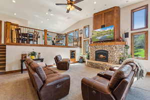 Carpeted living area with ceiling fan, a stone fireplace, vaulted ceiling, and recessed lighting
