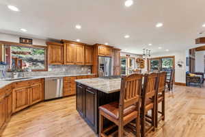 Kitchen featuring light stone countertops, a kitchen bar, light wood finished floors, wood finish cabinetry, and stainless steel appliances