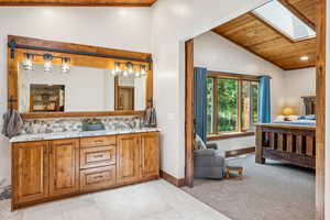 Full bathroom with a vaulted wooden ceiling, a skylight, double vanity, ensuite bathroom, and backsplash
