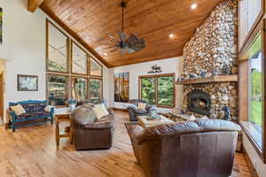 Living area with light wood finished floors, a vaulted wooden ceiling, a stone fireplace, plenty of natural light, and recessed lighting