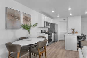 Kitchen featuring a kitchen breakfast bar, white cabinetry, stainless steel appliances, light wood-type flooring, and a peninsula