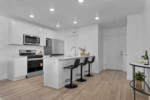Kitchen with a kitchen breakfast bar, stainless steel appliances, white cabinetry, a peninsula, and light wood-style flooring