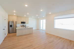 Kitchen with stainless steel appliances, a kitchen island with sink, recessed lighting, light wood finished floors, and open floor plan