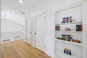 Hall with an upstairs landing, light wood-style flooring, recessed lighting, vaulted ceiling, and built in features