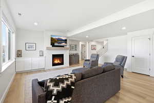 Living area featuring light wood-type flooring, a warm lit fireplace, and recessed lighting