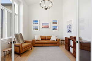 Living area with light wood finished floors, french doors, hanging lights, and a high ceiling