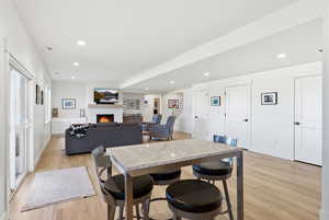 Dining room featuring light wood-style flooring, a warm lit fireplace, and recessed lighting