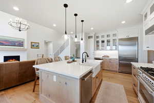 Kitchen featuring glass insert cabinets, premium appliances, a breakfast bar area, open floor plan, and light wood-type flooring