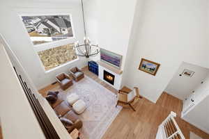 Living room with a high ceiling, light wood-type flooring, suspended lighting, and a warm lit fireplace