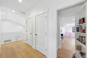 Corridor with vaulted ceiling, recessed lighting, light wood-style flooring, and an upstairs landing