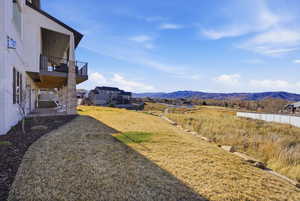 View of grassy yard with a patio, a mountain view, and a balcony