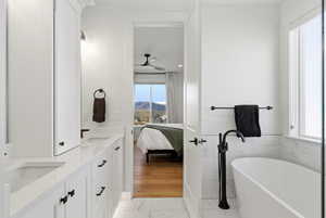 Full bath with ensuite bath, double vanity, a freestanding bath, light marble finish floors, and a mountain view