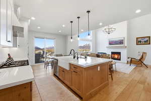 Kitchen featuring light wood-style flooring, a breakfast bar, an island with sink, a lit fireplace, and open floor plan