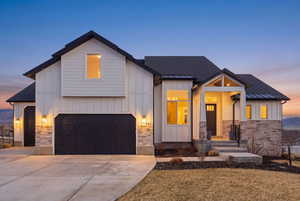 Modern inspired farmhouse featuring board and batten siding, a shingled roof, stone siding, and driveway