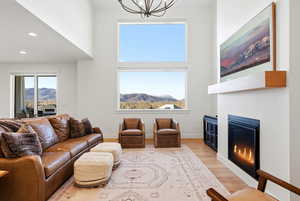 Living area featuring light wood-style flooring, a high ceiling, a glass covered fireplace, hanging lights, and a mountain view
