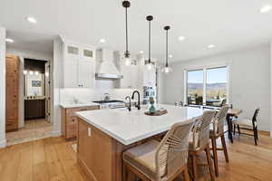 Kitchen featuring two tone cabinets, light wood-style floors, a center island with sink, glass insert cabinets, and a breakfast bar