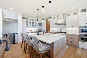 Two tone kitchen featuring glass fronted cabinets, a kitchen island with sink, light wood finished floors, a breakfast bar area, and two tone cabinets