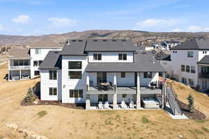 Back of house featuring a hot tub, a patio, a residential view, a mountain view, and a shingled roof