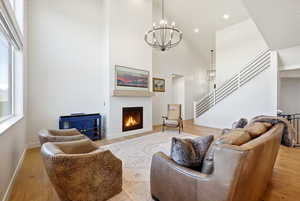 Living room with light wood-style flooring, a chandelier, a warm lit fireplace, and a high ceiling