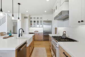 Kitchen with glass fronted cabinets, premium appliances, light wood-style floors, light stone countertops, and two tone color scheme