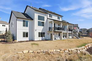 Rear view of house with a patio, a balcony, a yard, a shingled roof, and board and batten siding