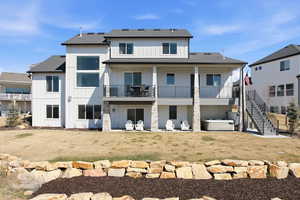 Back of property with a patio area, a hot tub, a shingled roof, board and batten siding, and a balcony