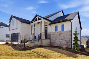 Modern inspired farmhouse with board and batten siding, a front lawn, roof with shingles, stone siding, and an attached garage