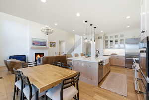 Dining area featuring light wood-type flooring, a warm lit fireplace, and hanging lights