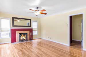 Bright living room featuring a cozy fireplace with a decorative hearth and  warm wood floors. Colors may be updated in person.