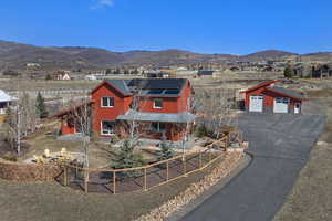 Rustic home with solar panels, a garage, an outbuilding, a mountain view, and driveway