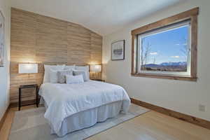 Bedroom with light wood-style flooring, vaulted ceiling, and an accent wall