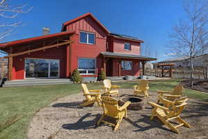 Rear view of property featuring a patio area, a lawn, a chimney, roof mounted solar panels, and board and batten siding