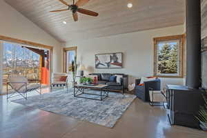 Living area with a wood stove, a vaulted wooden ceiling, a ceiling fan, concrete flooring, and recessed lighting