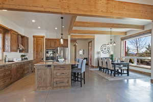 Kitchen featuring an island with sink, wood finish cabinetry, light stone countertops, finished concrete floors, and decorative backsplash