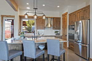 Kitchen featuring stainless steel appliances, light stone countertops, backsplash, pendant lighting, and a textured ceiling