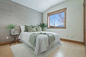 Bedroom with an accent wall, light wood-style floors, and vaulted ceiling