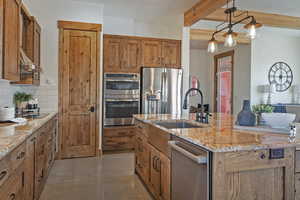 Kitchen with wood finish cabinetry, stainless steel appliances, a center island with sink, hanging light fixtures, and beamed ceiling