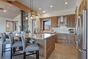 Kitchen featuring wood finish cabinets, light stone counters, freestanding refrigerator, decorative backsplash, and lofted ceiling with beams