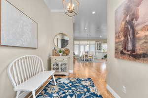 Hallway with suspended lighting, crown molding, and light wood-style floors