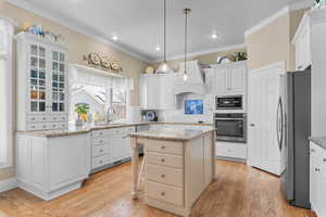 Kitchen with a breakfast bar area, stainless steel appliances, a center island, light wood-type flooring, and white cabinetry