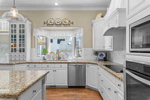 Kitchen featuring stainless steel appliances, white cabinetry, light wood-style flooring, light stone countertops, and crown molding