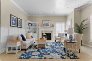 Living area with light carpet, a premium fireplace, ornamental molding, and wainscoting