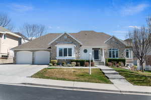 View of front of home with stone siding, a garage, concrete driveway, roof with shingles, and a front yard