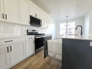 Kitchen with stainless steel appliances, white cabinets, light wood-type flooring, light stone counters, and decorative backsplash