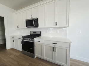 Kitchen with stainless steel appliances, white cabinetry, dark wood-type flooring, and light stone counters